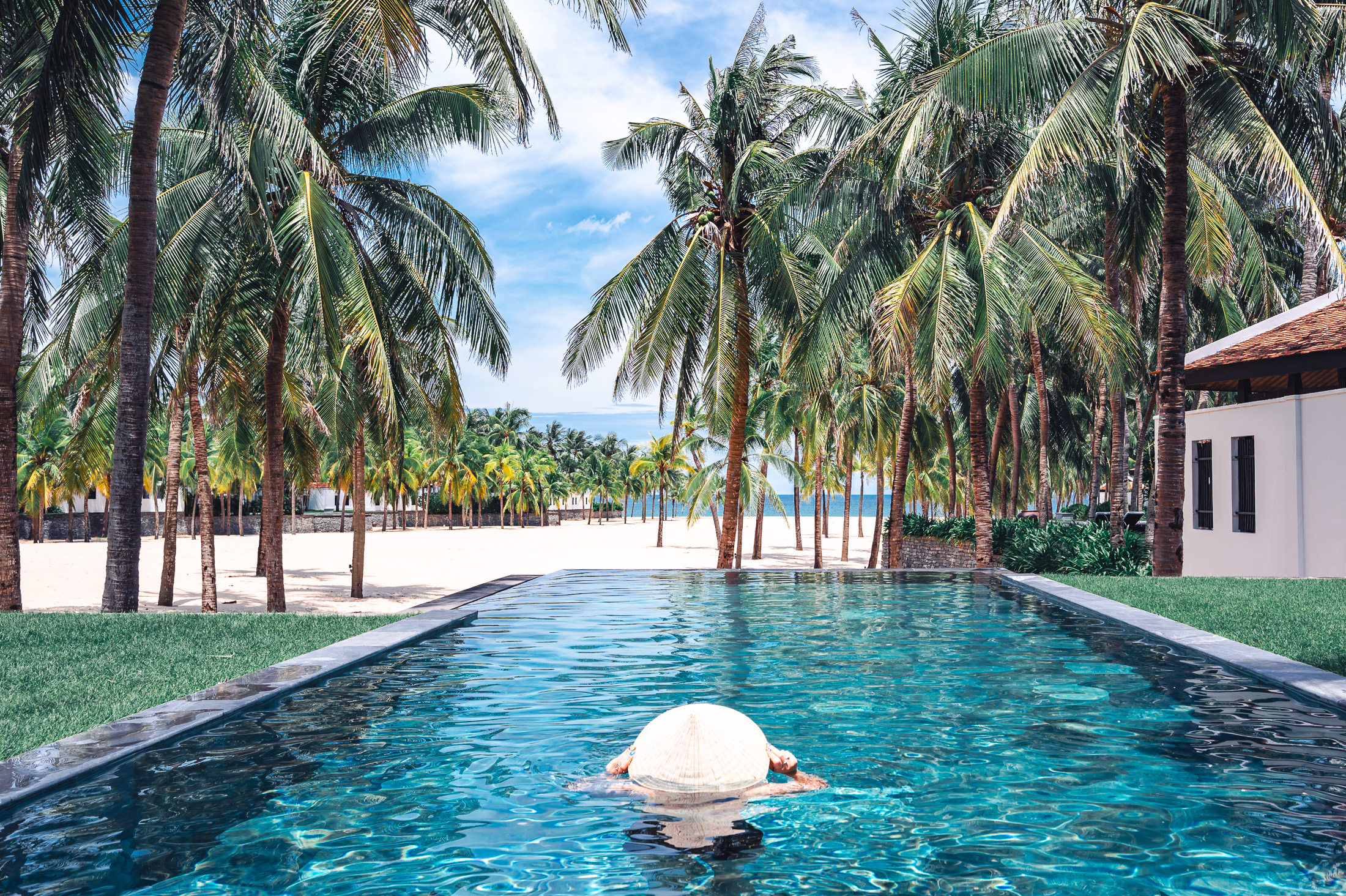 A woman wearing a Vietnamese conical hat while paddling in The private pool at the Four Seasons Nam Hai